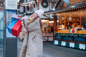 A smiling woman holding shopping bags at a holiday market.