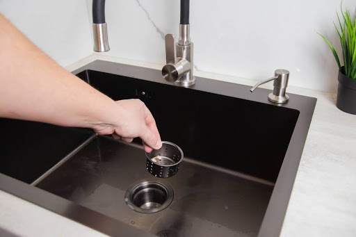 A hand putting a metal strainer into a kitchen sink drain.