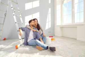 A smiling couple sitting on the floor near a ladder during a home renovation.