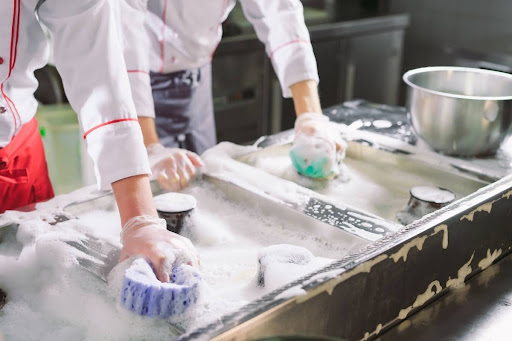 Cooks washing a sink and other equipment in a kitchen.