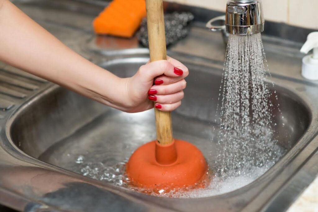 A woman using a plunger to unclog a sink.