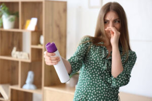 A woman covering her nose due to a bad smell and using an air freshener in a home.