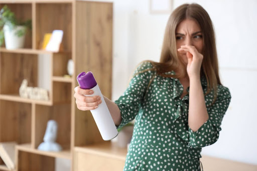 A woman covering her nose due to a bad smell and using an air freshener in a home.